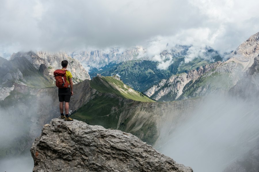 Hiker with a red backpack standing on a cliff facing misty mountains